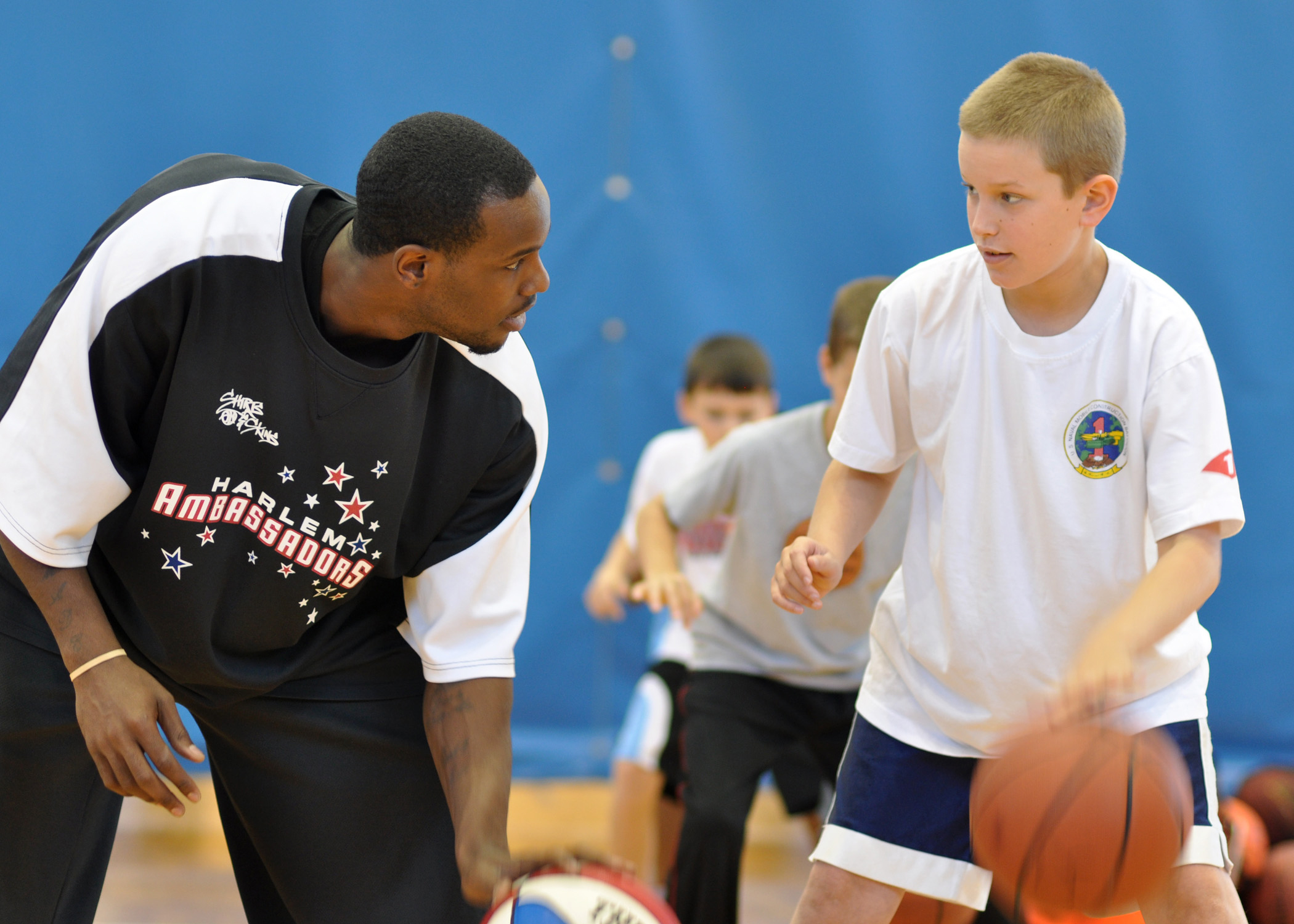 An adult demonstrating basketball dribbling technique beside a child at a youth clinic