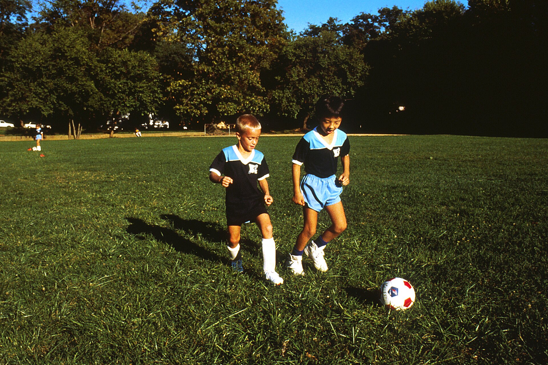 Two children approaching a football on grass while practising close control outdoors