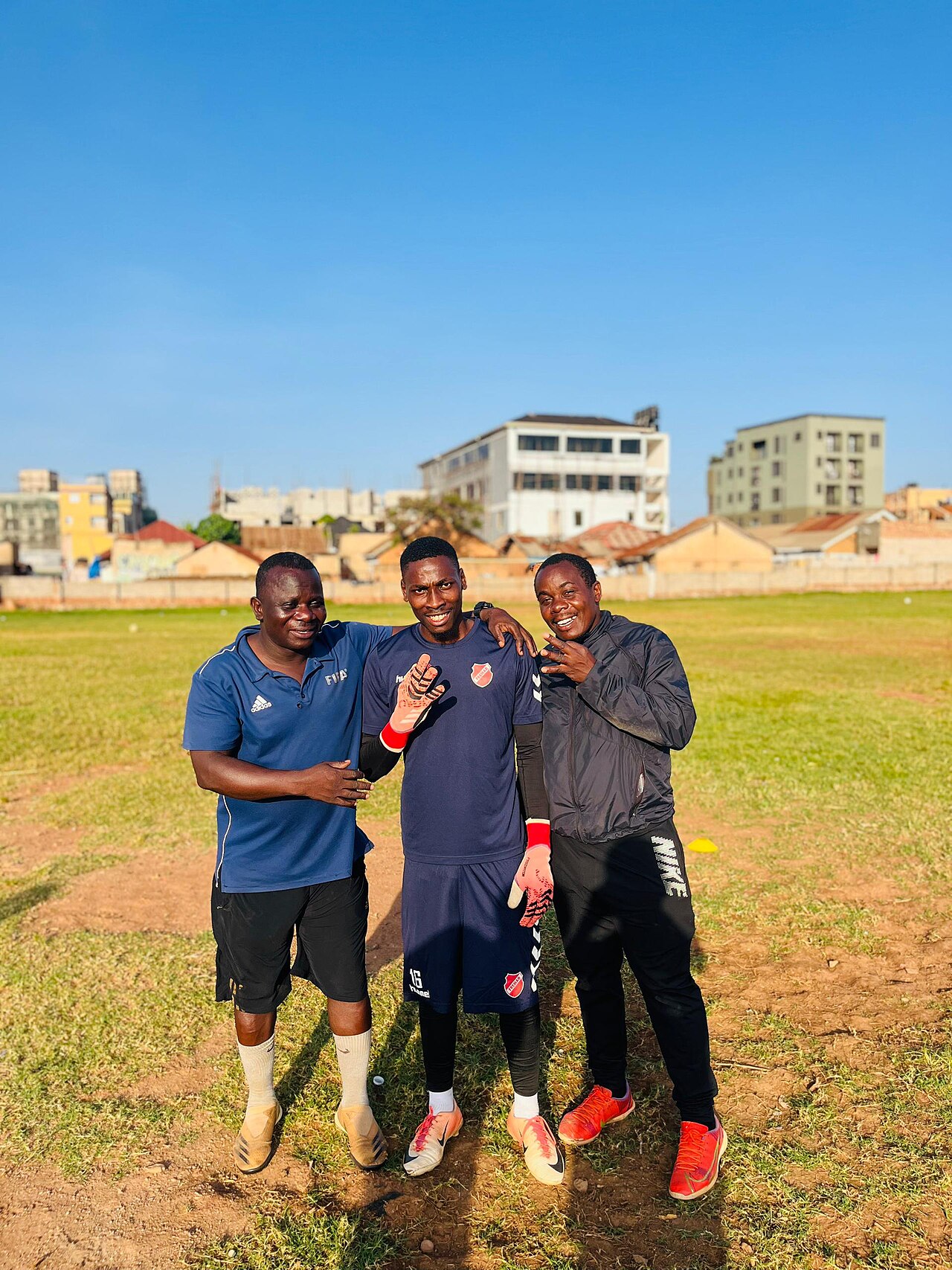Goalkeeper in gloves standing with two coaches on a football training field, with all three people's feet visible
