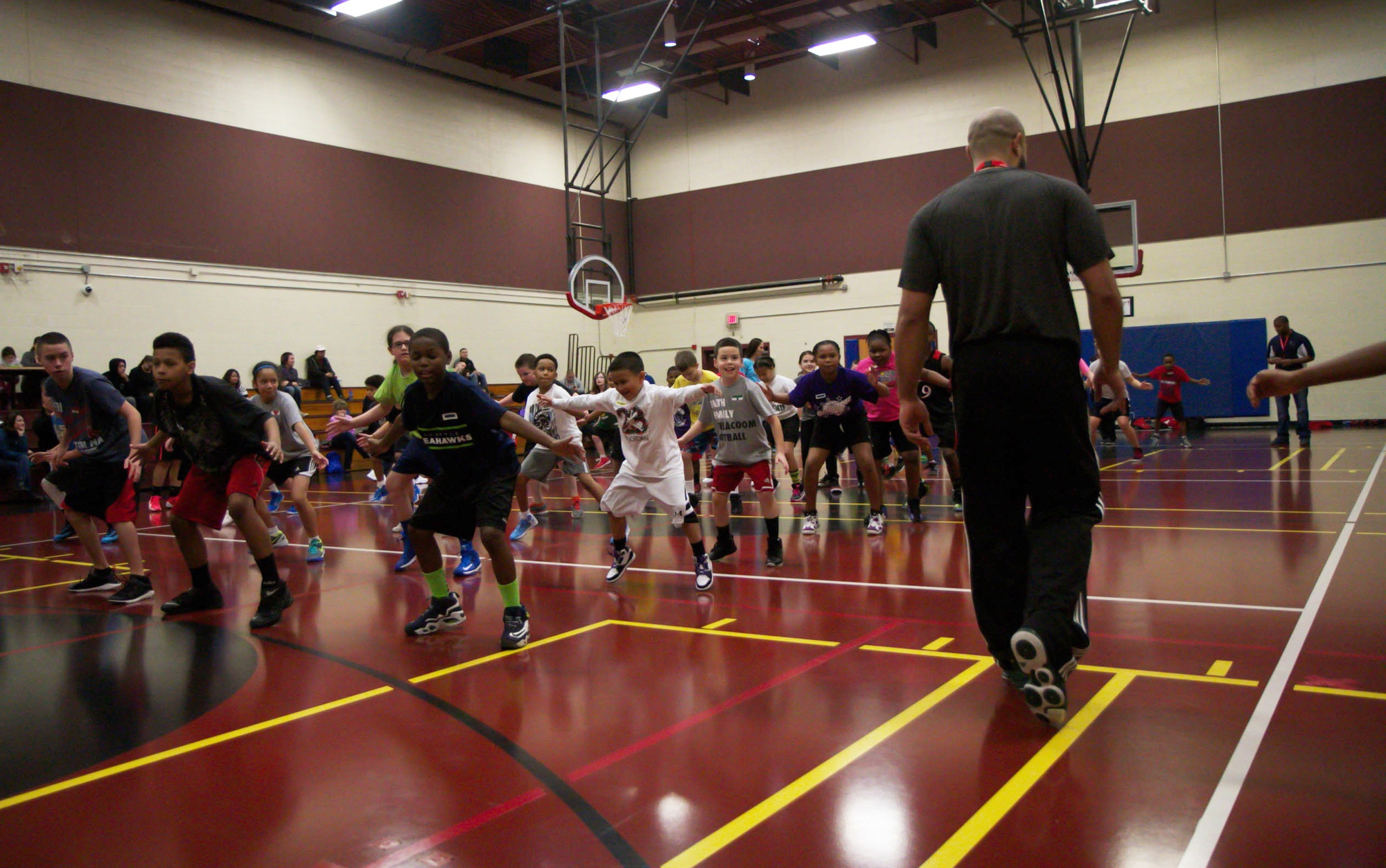 Children practising balanced athletic movement while an adult leader supervises a youth basketball clinic