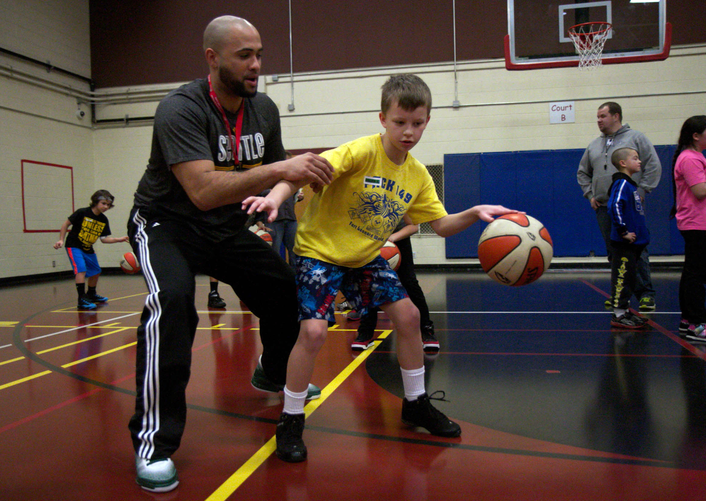 Child dribbling in a low stance while an adult coach applies light pressure during a youth basketball clinic